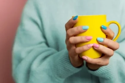 A woman has grabbed a yellow cup with his hand and beautiful Nails