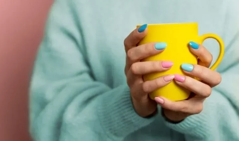 A woman has grabbed a yellow cup with his hand and beautiful Nails