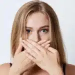 a woman has covereed her mouth with both her hands to prevent bad breath