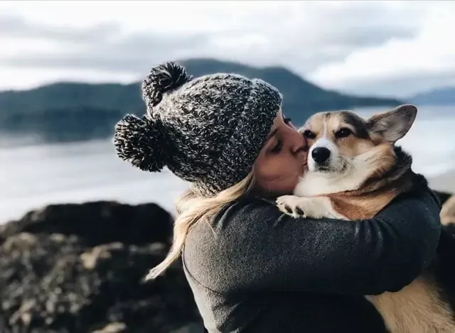 A girl is holding a dog and kissing him