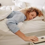 A girl lying in the bed is holding a mobile.