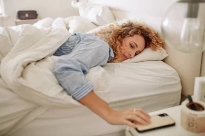 A girl lying in the bed is holding a mobile.