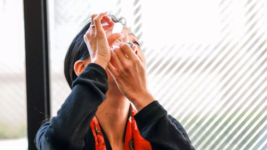 A woman putting eye drops in her eyes